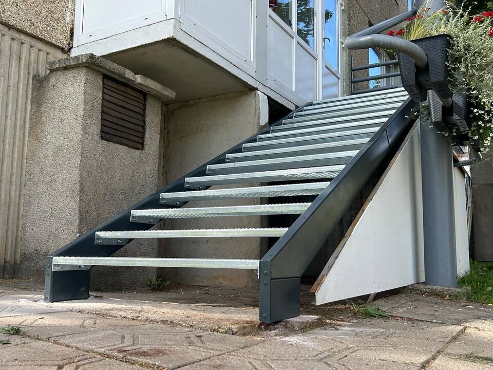 Utvendig ståltrapp med galvaniserte trinn langs betongfasade